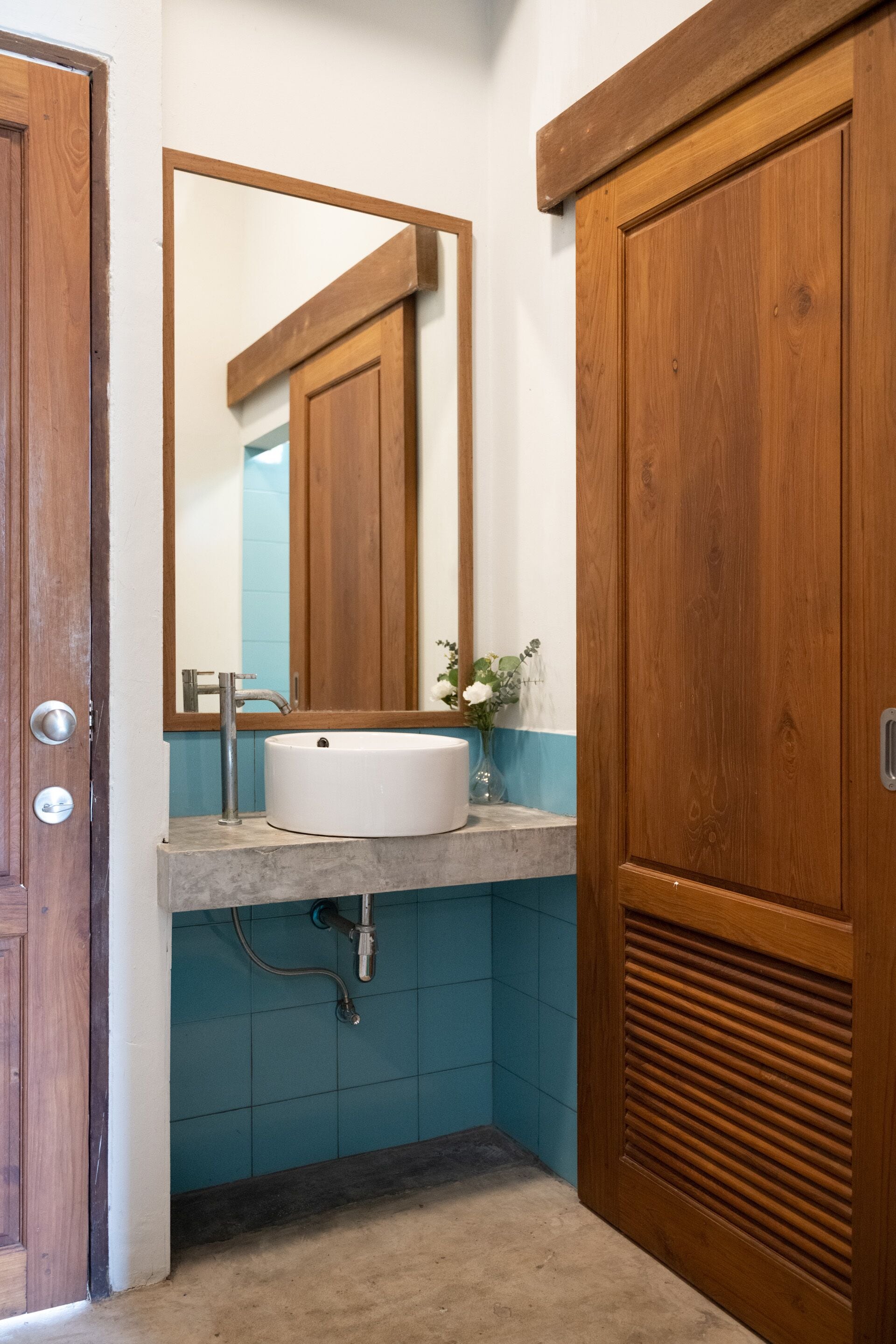 A bathroom with a wooden door, a white sink, a mirror, and a blue tiled wall.