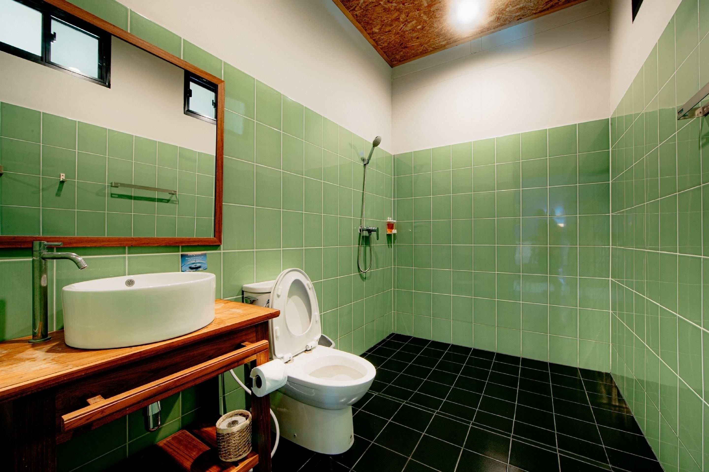 A bathroom with green tiles, a white sink, a toilet, and a shower.