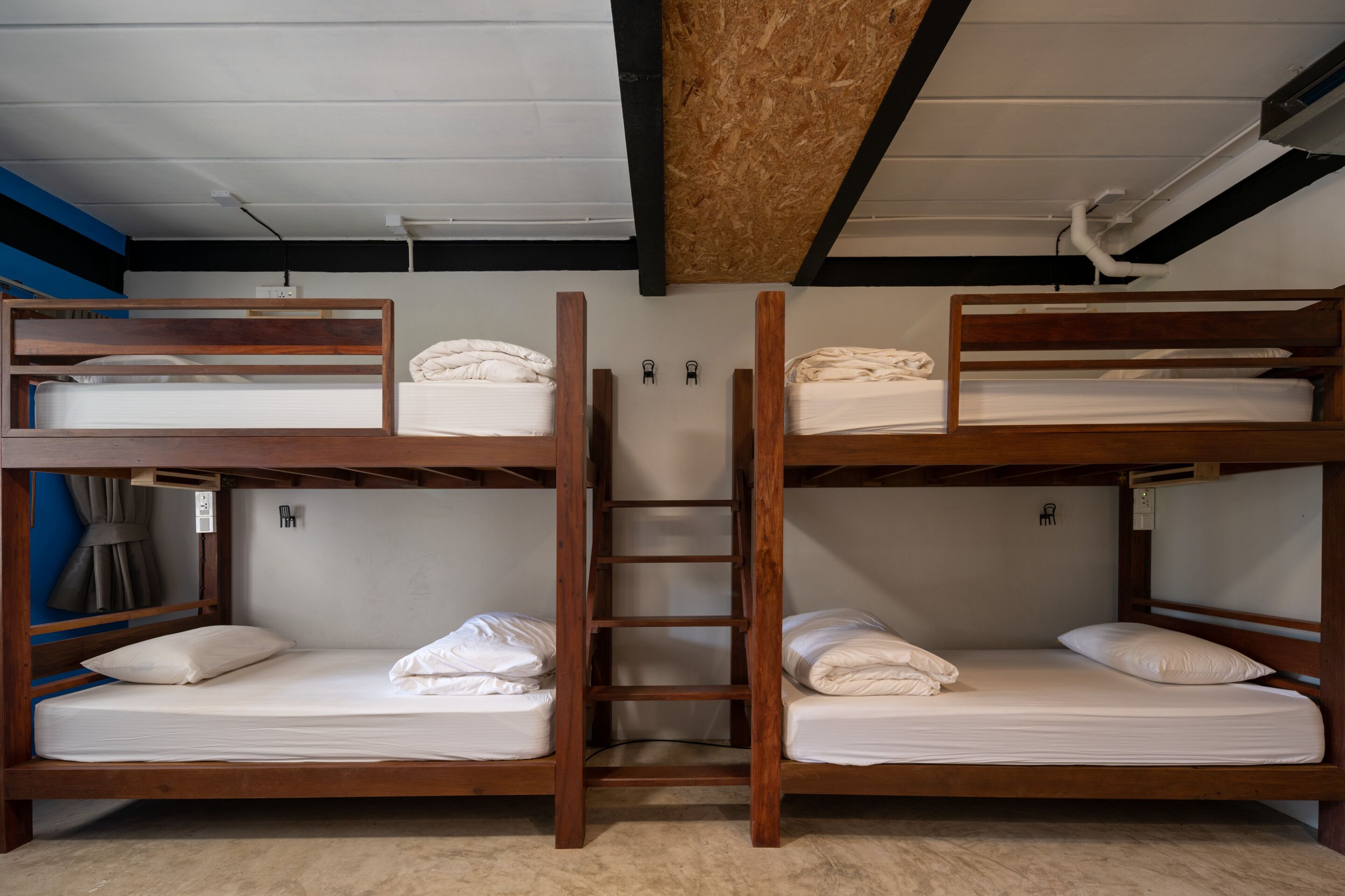A bunk bed room with a wooden ladder, white bedding, and a blue wall.
