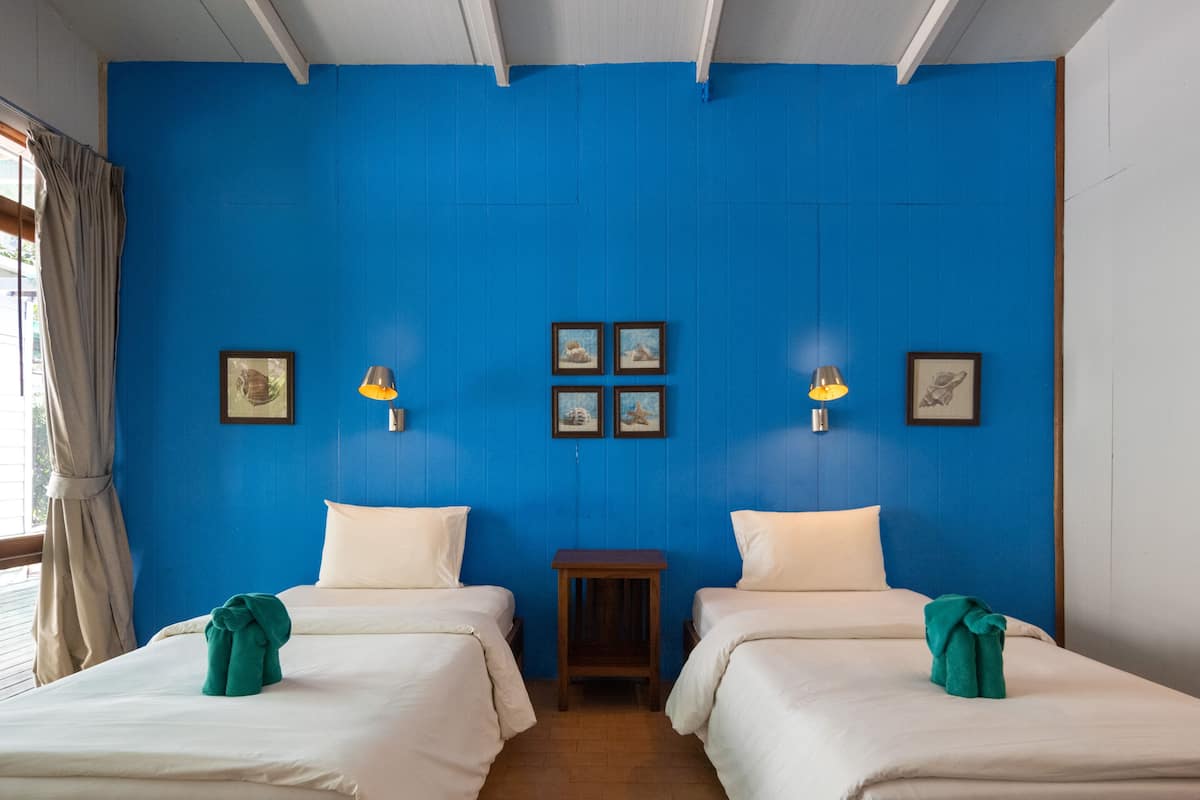 Una habitación con dos camas, una mesita pequeña y una pared azul decorada con cuadros.