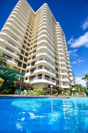Un hotel de gran altura con múltiples balcones, piscina y abundante vegetación.
