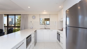 Una cocina moderna con armarios blancos, un refrigerador de acero inoxidable y una ventana con vistas a edificios y árboles.