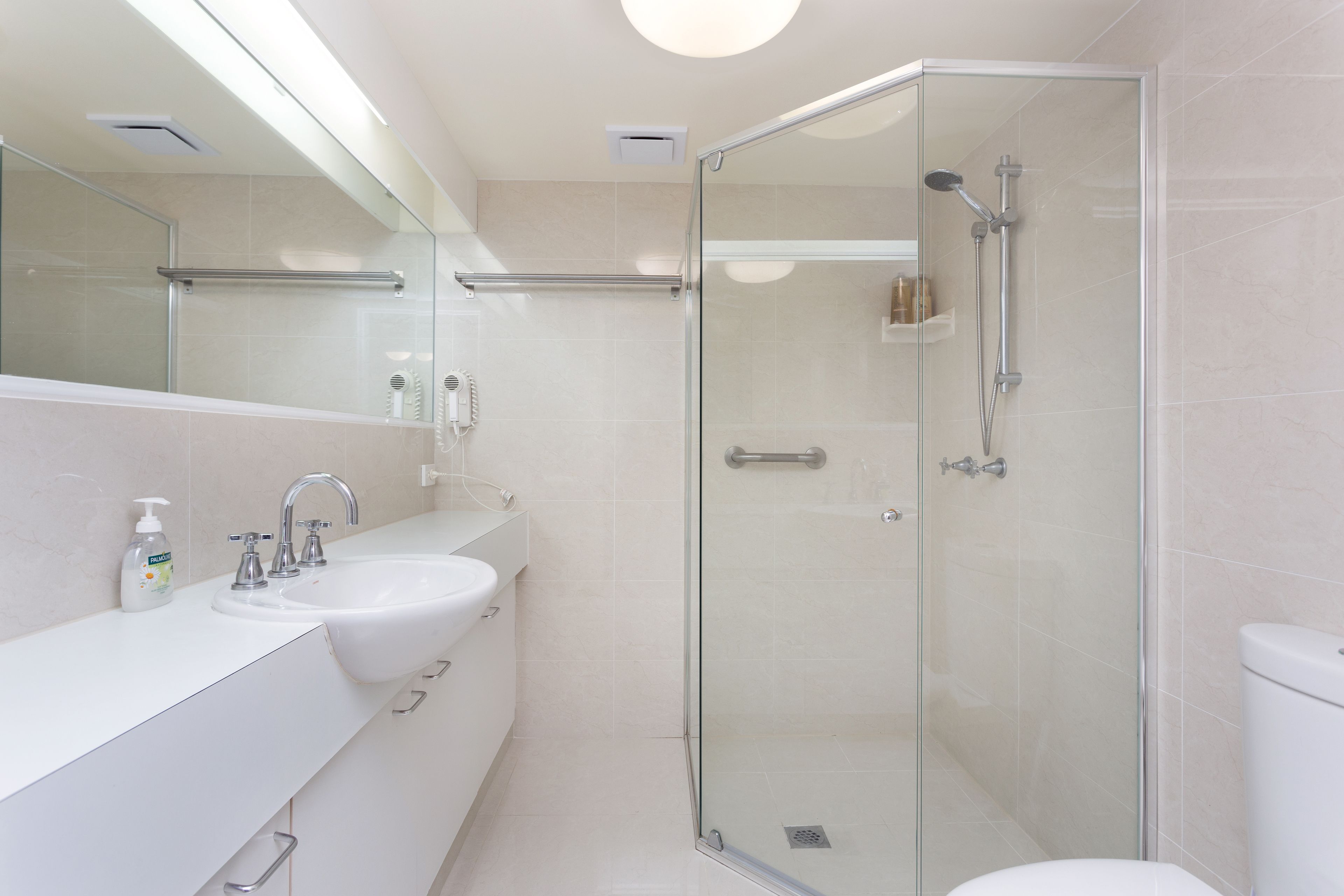 A modern bathroom with a glass-enclosed shower, a white sink, and a large mirror.