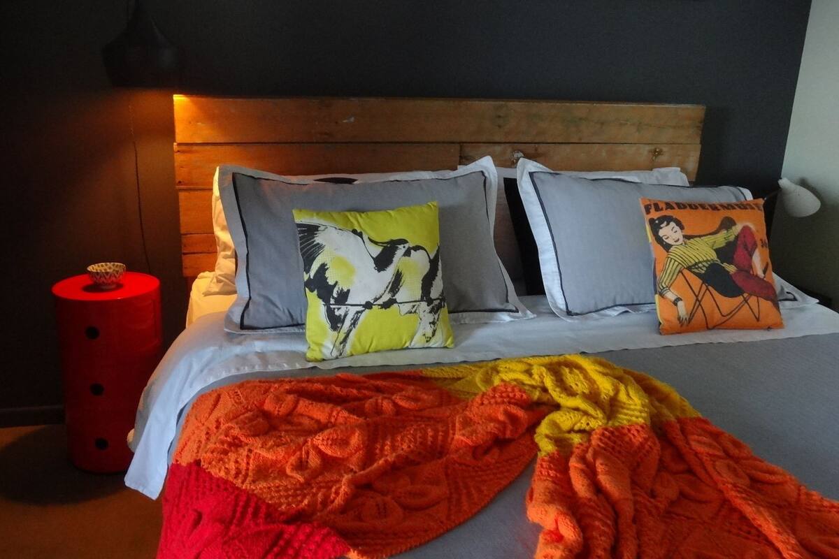 A bed with a wooden headboard, two pillows with a black and white design, and a colorful blanket.