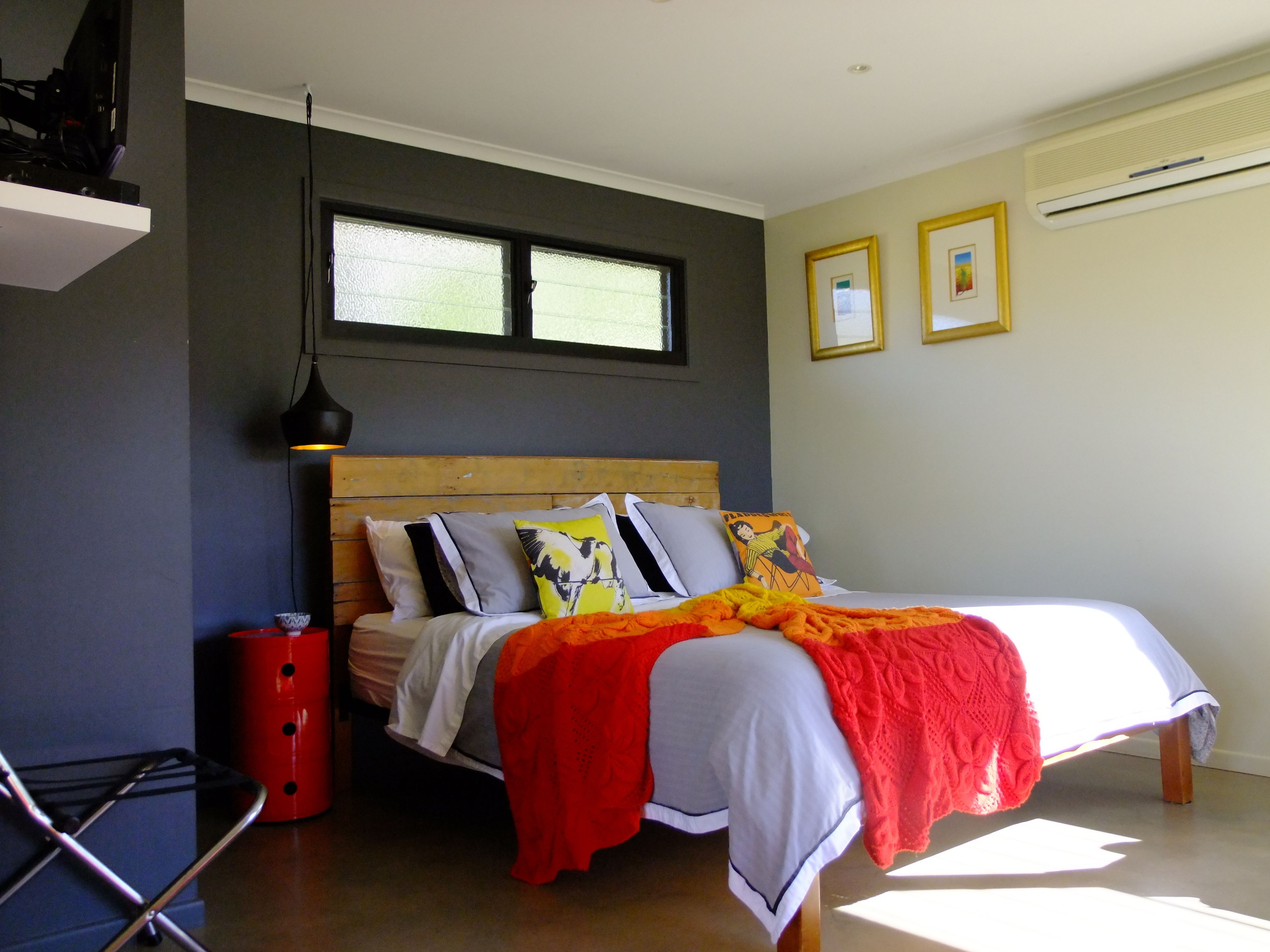 Ein Schlafzimmer mit einem hölzernen Bett, einem roten Nachttisch, einem Fenster und zwei gerahmten Bildern an der Wand.