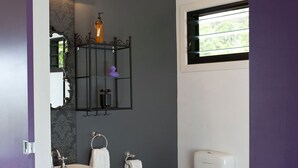 Un baño con lavamanos, inodoro y bañera blancos. Hay un taburete de madera pequeño y un espejo con marco decorativo.