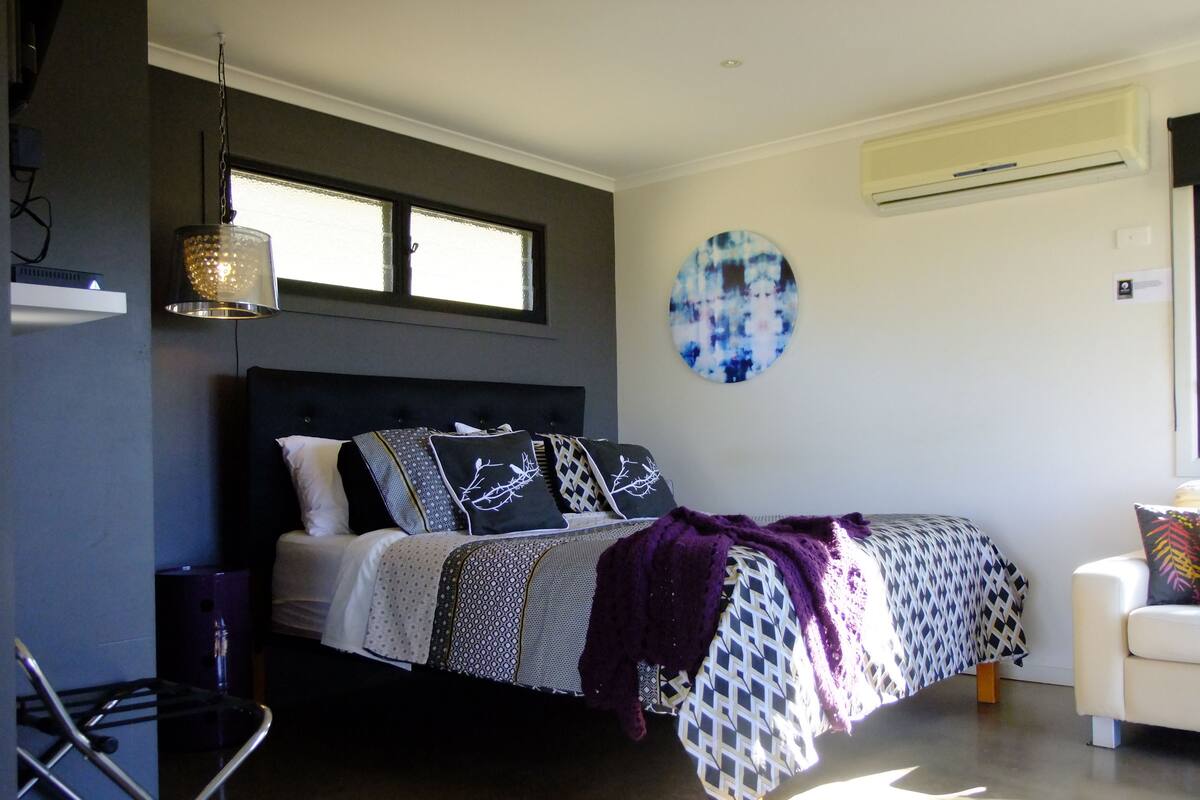 A modern bedroom with a bed, a chair, a hanging light, and a round wall decoration.