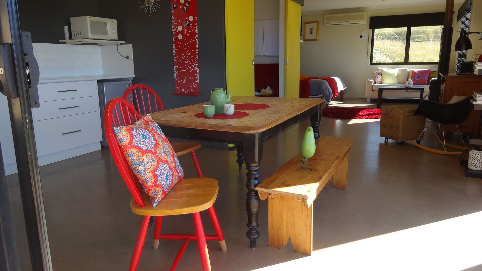 Una cocina moderna con comedor, que incluye una mesa de madera, sillas rojas y un colorido adorno en la pared.