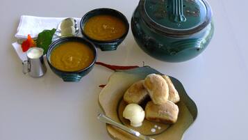 Un tavolo con tre ciotole di zuppa, un teiera, un piatto con pane e burro, e una piccola brocca.