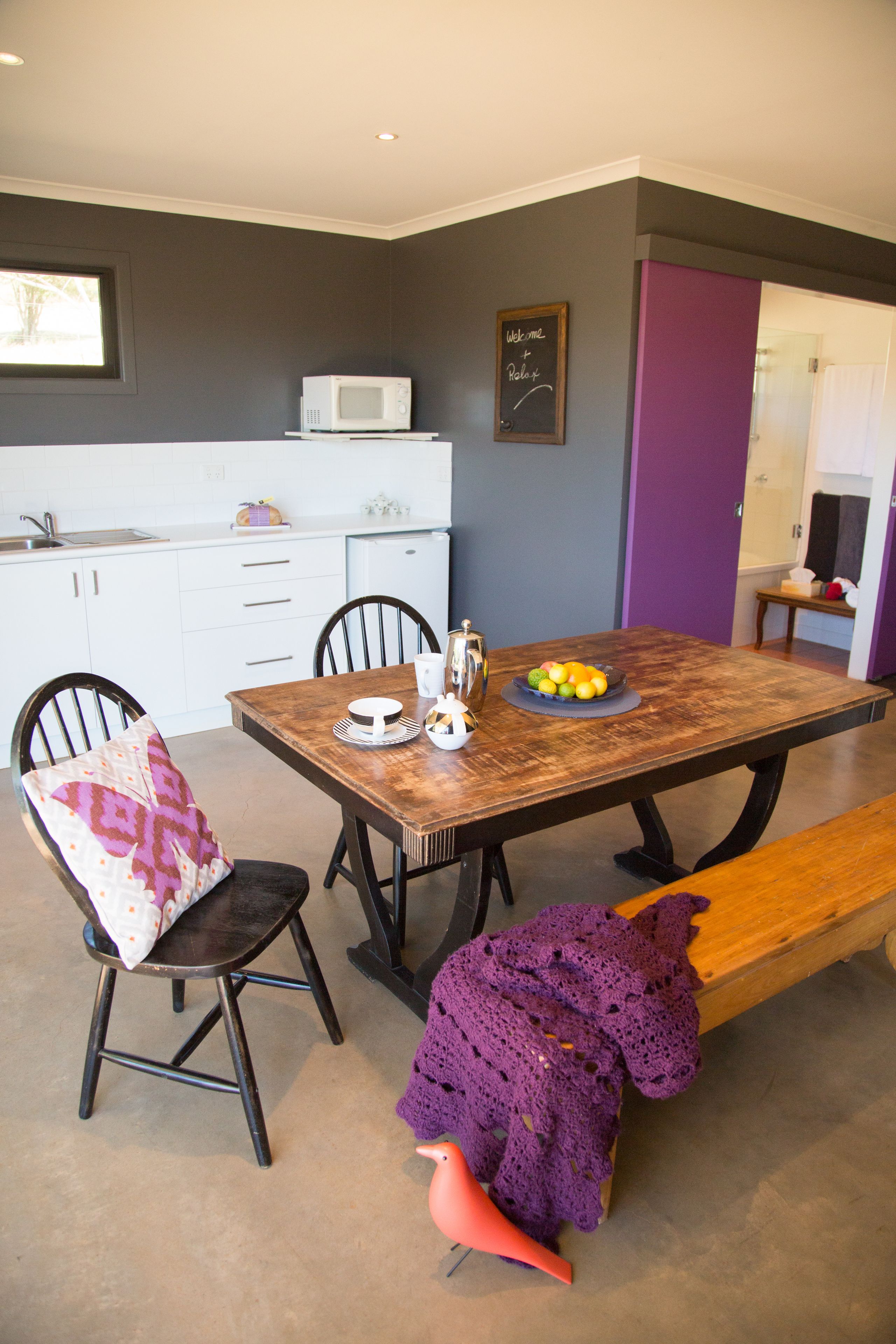 Un coin repas avec une table en bois, des chaises, un banc et une couverture violette tricotée.