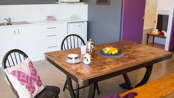 Un coin repas avec une table en bois, des chaises, un banc et une couverture violette tricotée.