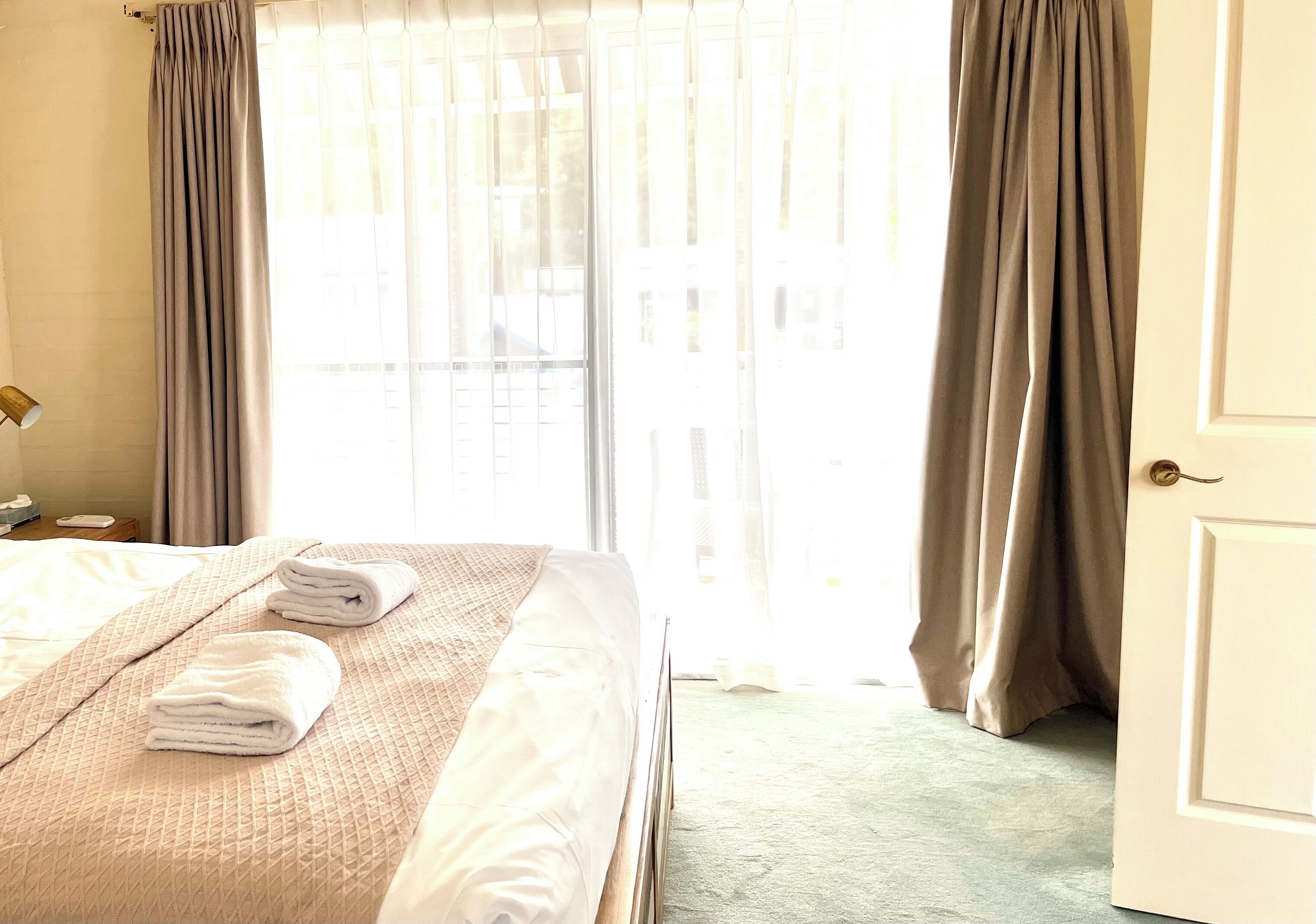 A hotel room with a bed, towels, curtains, and a door.