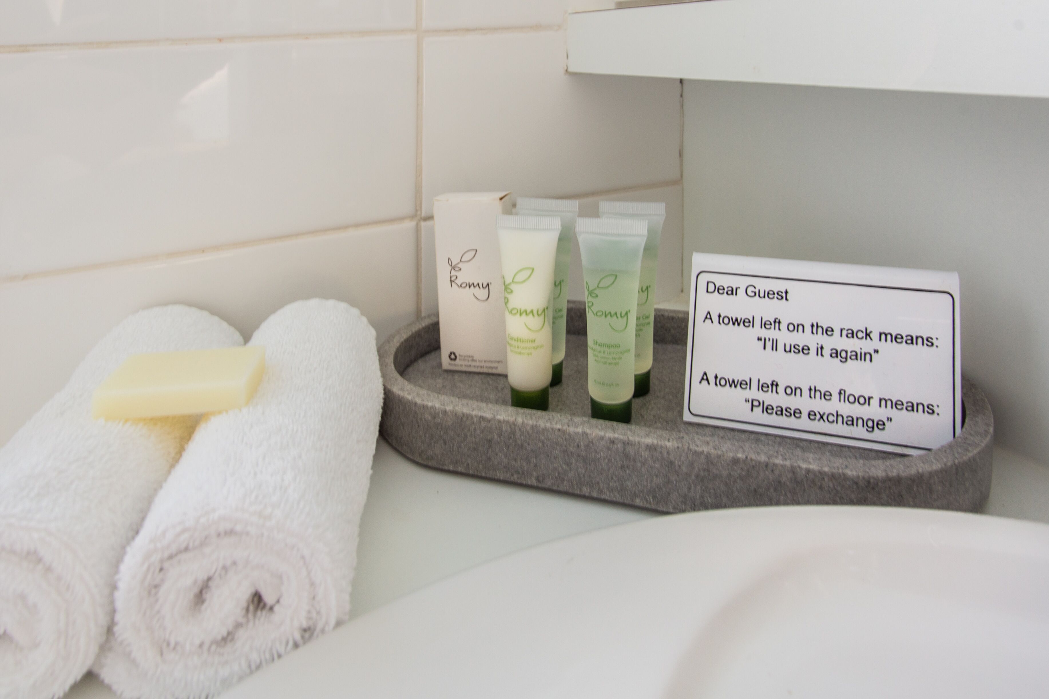 A bathroom with toiletries, a sign explaining towel usage, and neatly rolled towels.