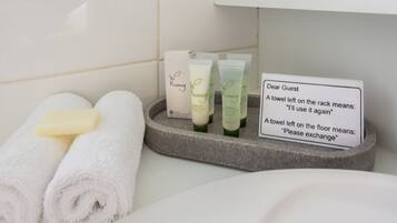 A bathroom with toiletries, a sign explaining towel usage, and neatly rolled towels.