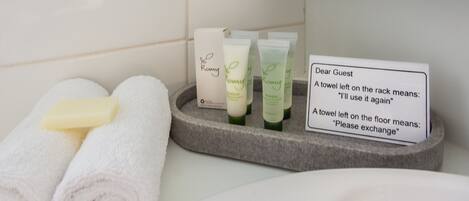 A bathroom with toiletries, a sign explaining towel usage, and neatly rolled towels.