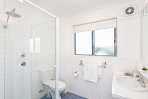 A modern bathroom with a glass-enclosed shower, a toilet, a sink, and a window providing natural light.