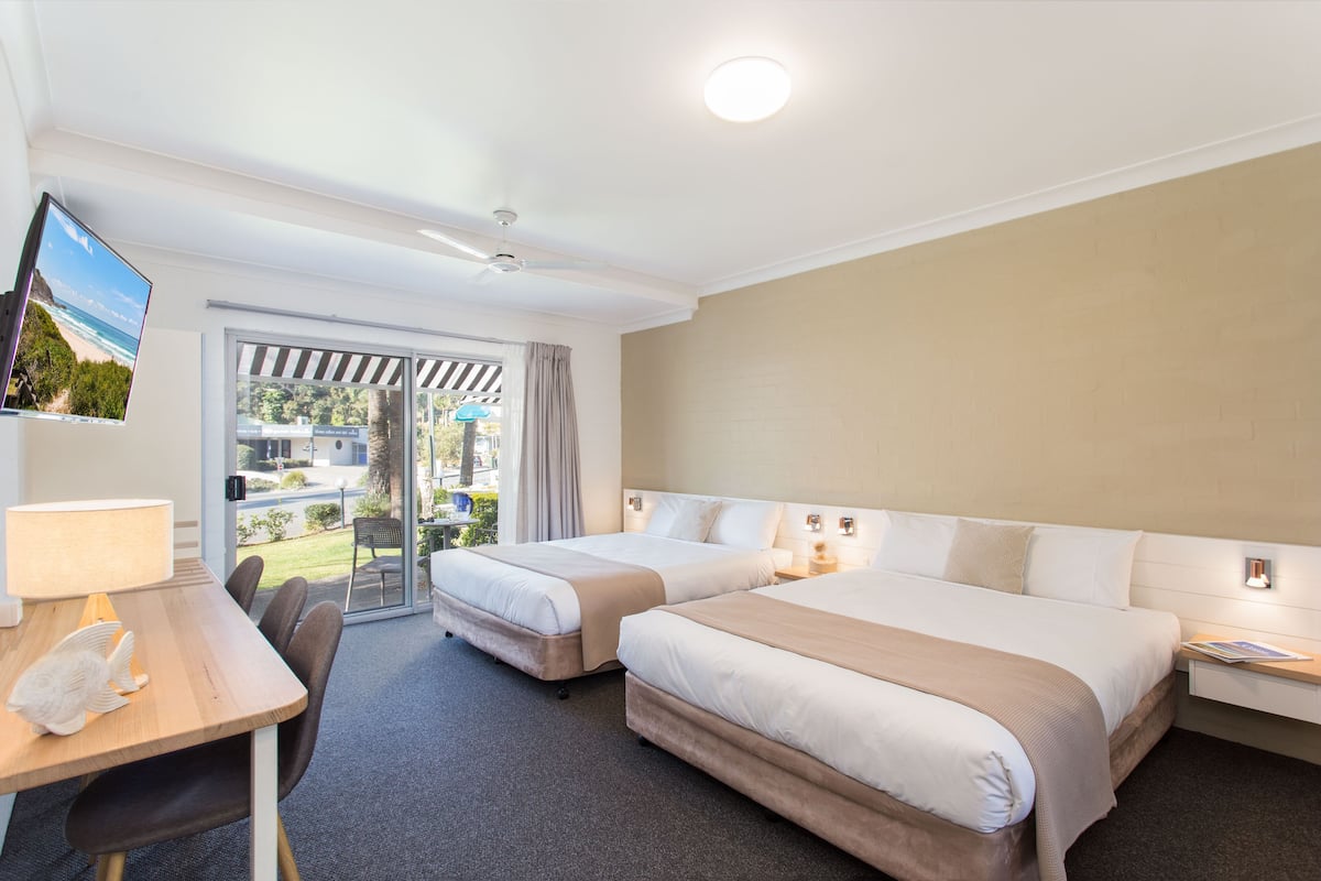 A hotel room with two beds, a desk with a lamp, a television, and a view of the outdoors.