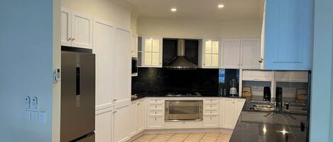 A modern kitchen with white cabinets, a black countertop, a built-in oven, and a skylight.