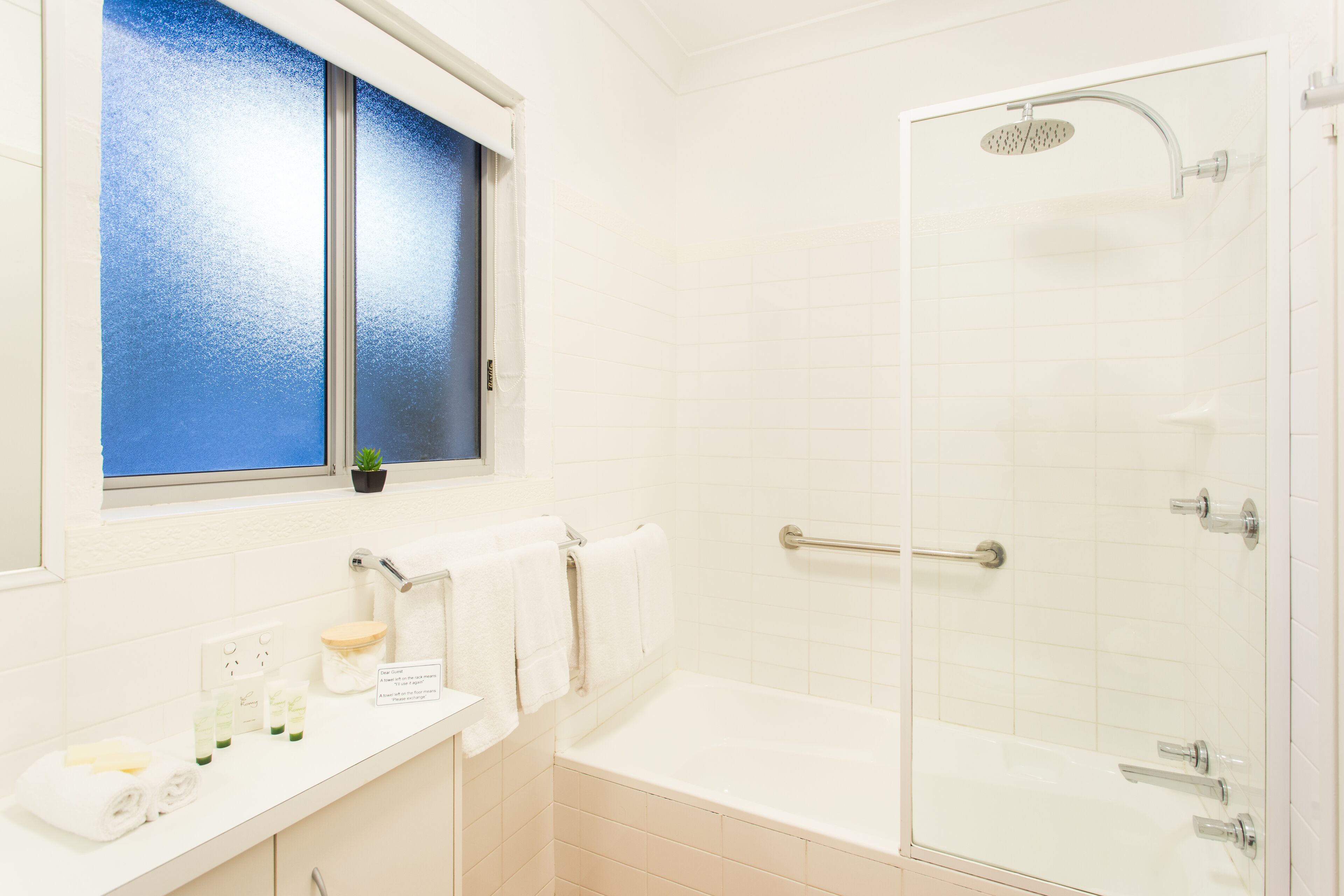 Un baño con bañera, ducha, ventana con vidrio esmerilado y zona de lavabo con artículos de aseo.