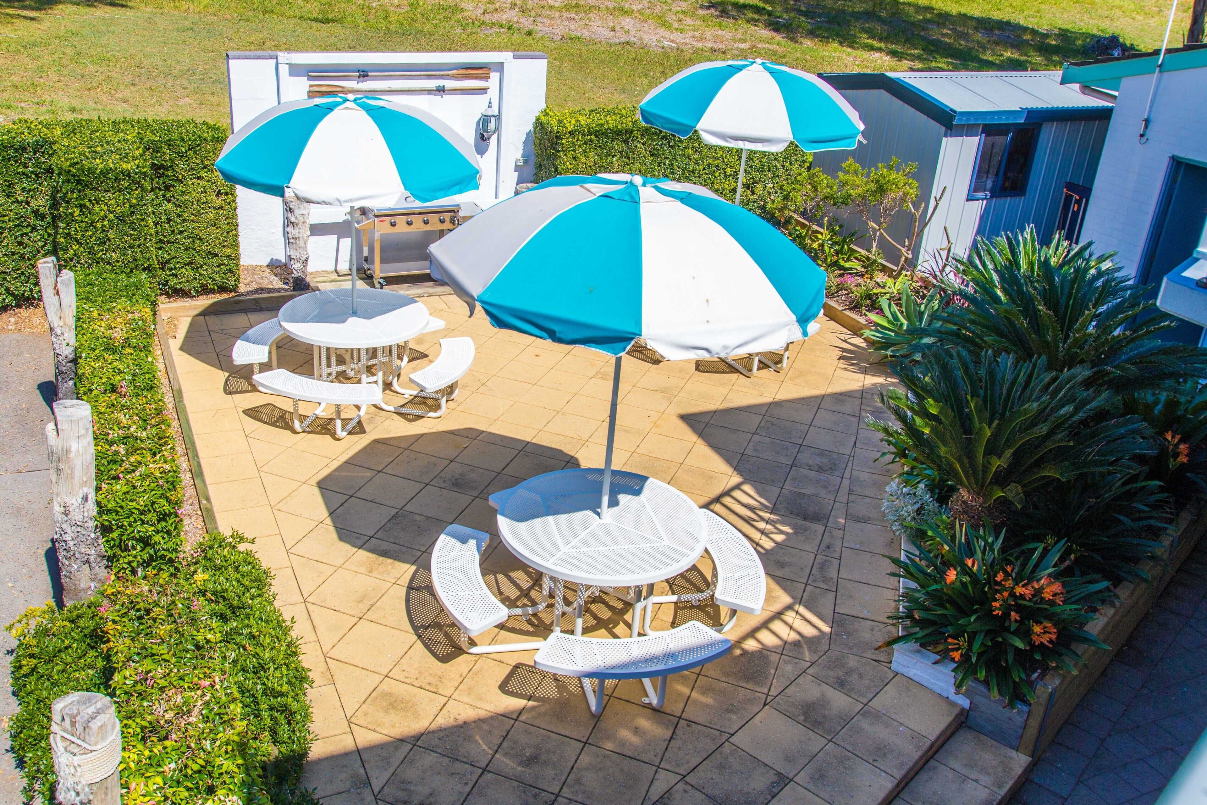 Een terras met buitenmeubilair en parasols, omringd door een haag en een gebouw.