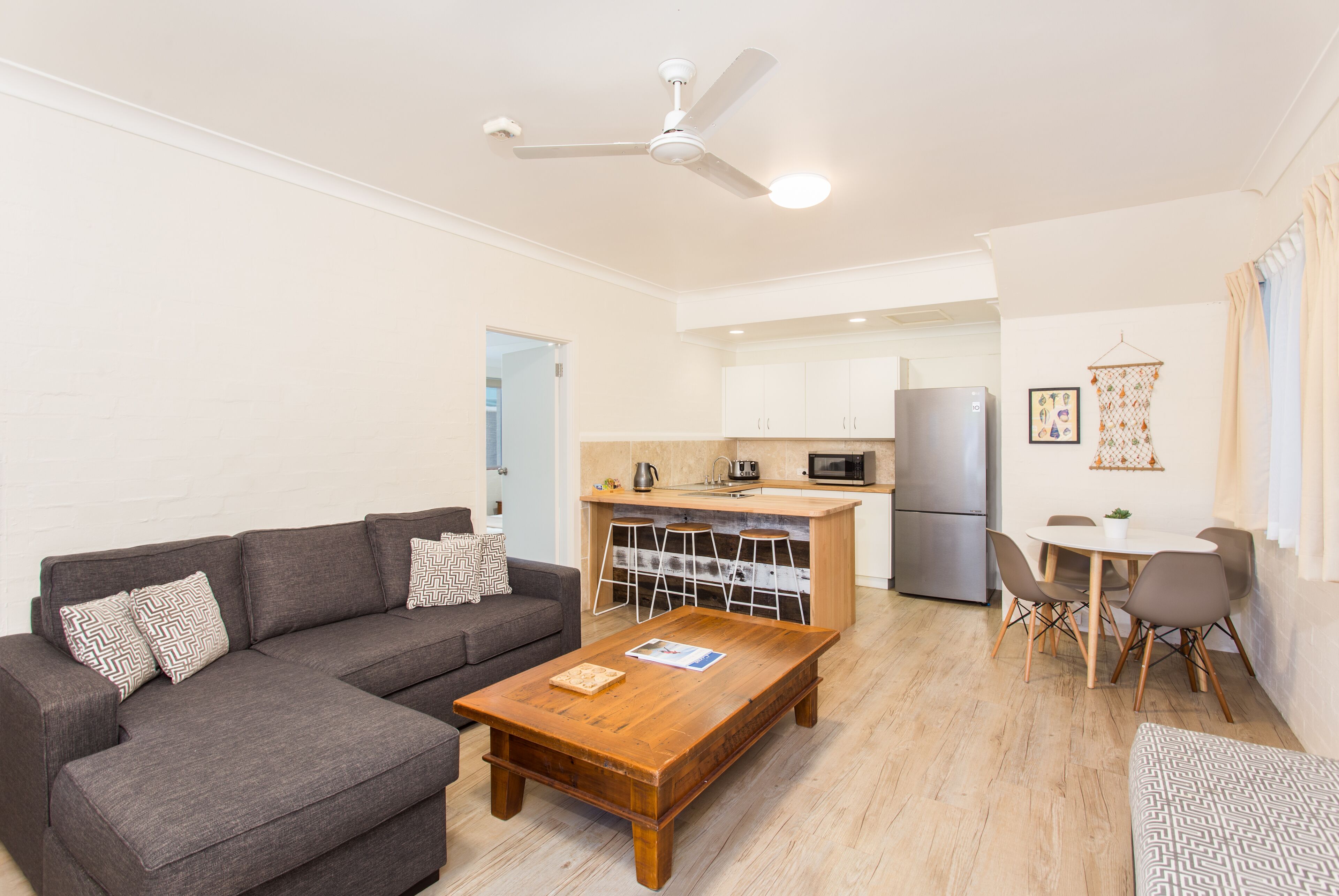 A living room with a sofa, coffee table, and a kitchen area with a refrigerator, microwave, and bar stools.