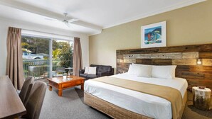 Habitación de hotel con una cama grande, un escritorio, una silla, un balcón con cortinas y un cuadro en la pared.