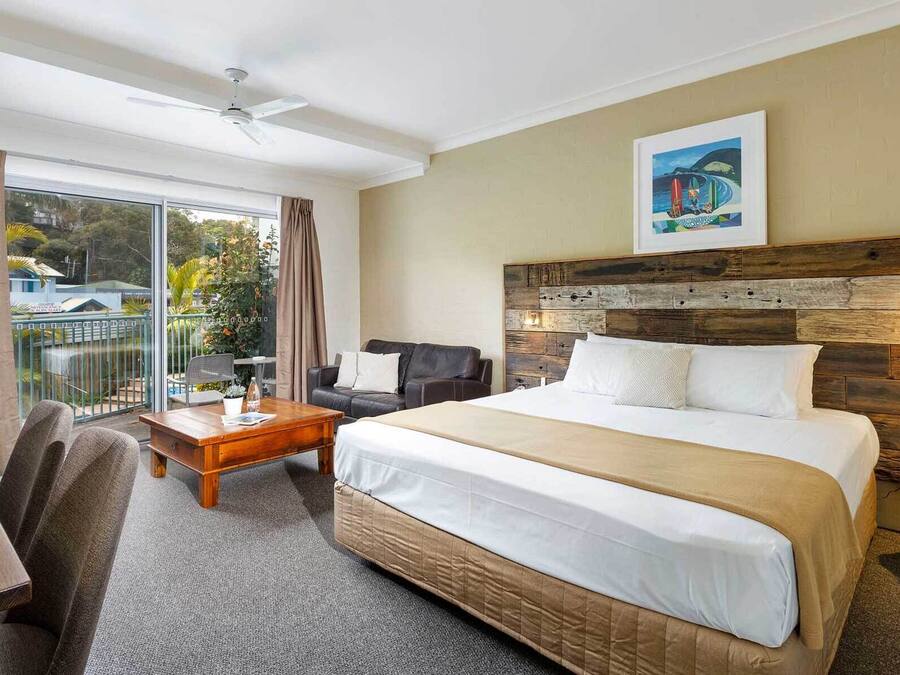 Een hotelkamer met een groot bed, een bureau, een stoel, een balkon met gordijnen en een schilderij aan de muur.