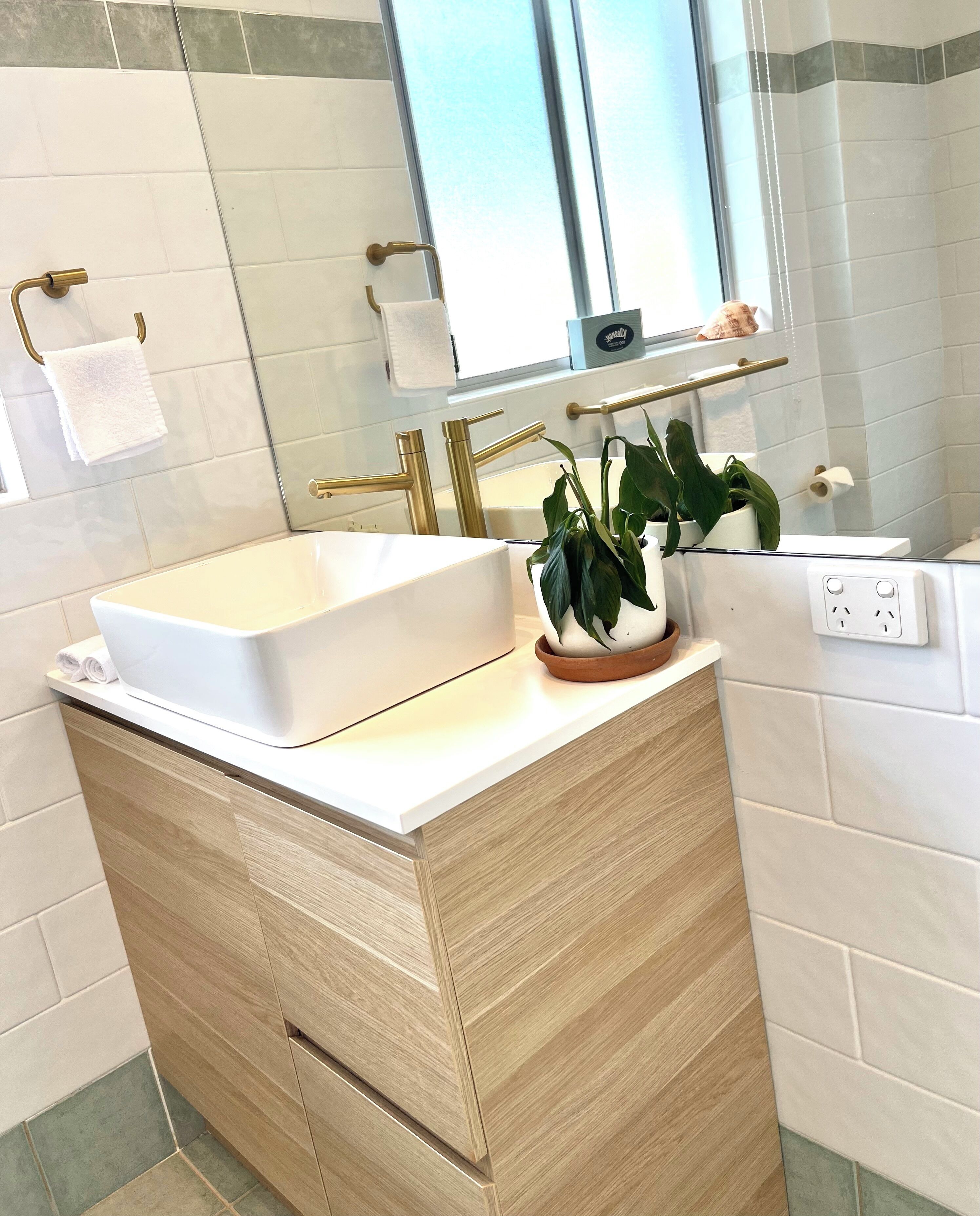 Un baño con lavamanos blanco, detalles dorados, un espejo y una planta en maceta.