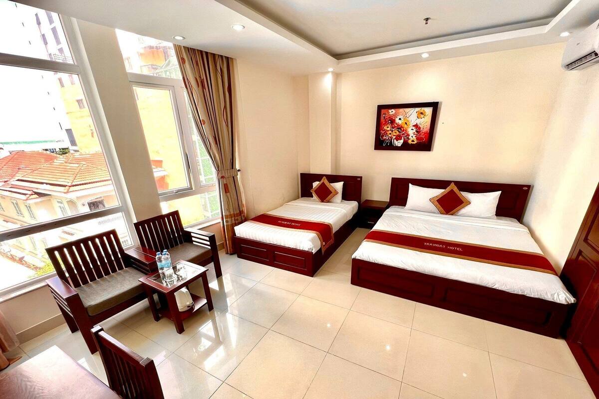 A hotel room with two beds, a dining table, chairs, and a large window with curtains.