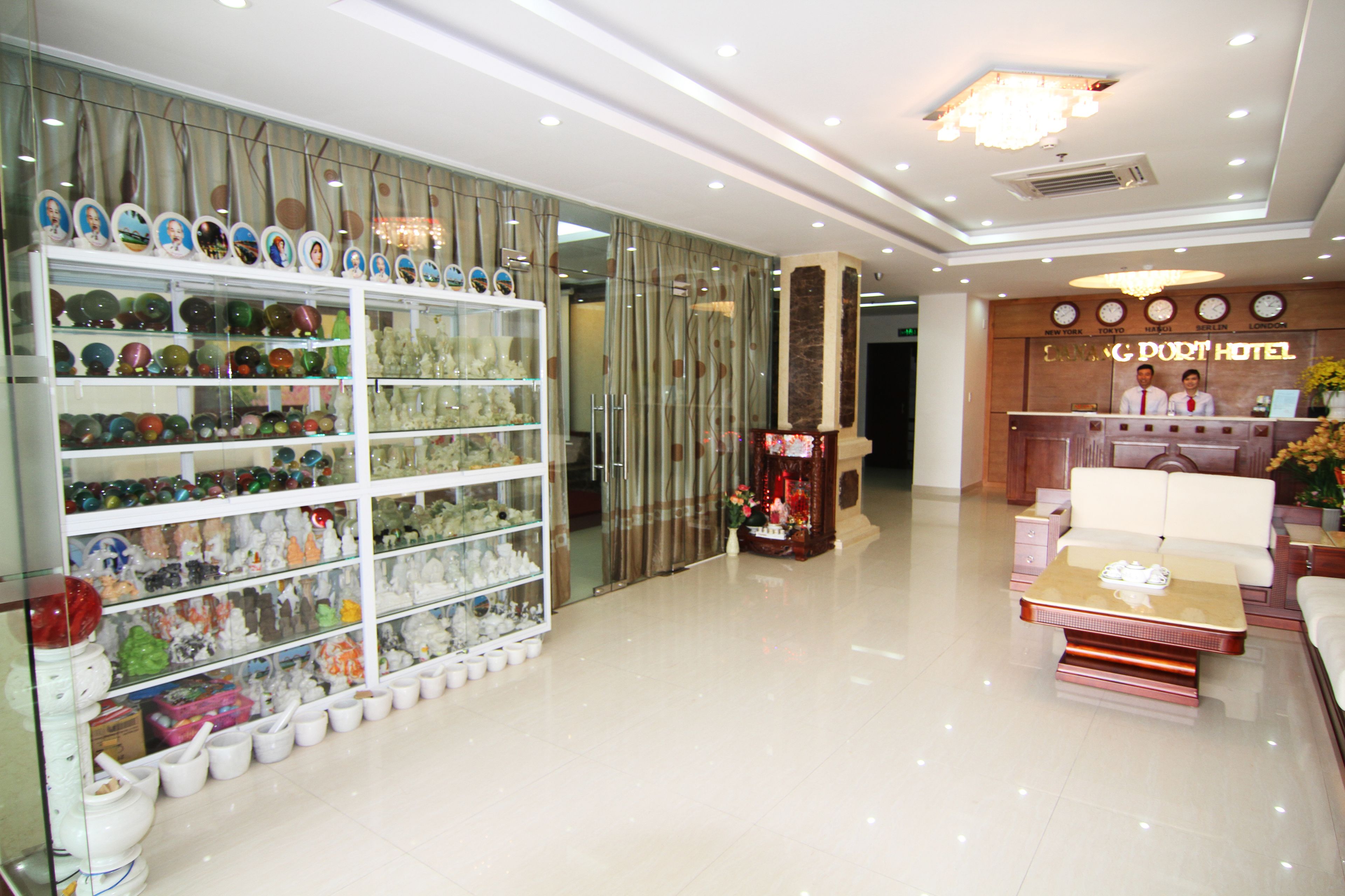 A hotel lobby with a reception desk, a glass display of decorative items, and a seating area.