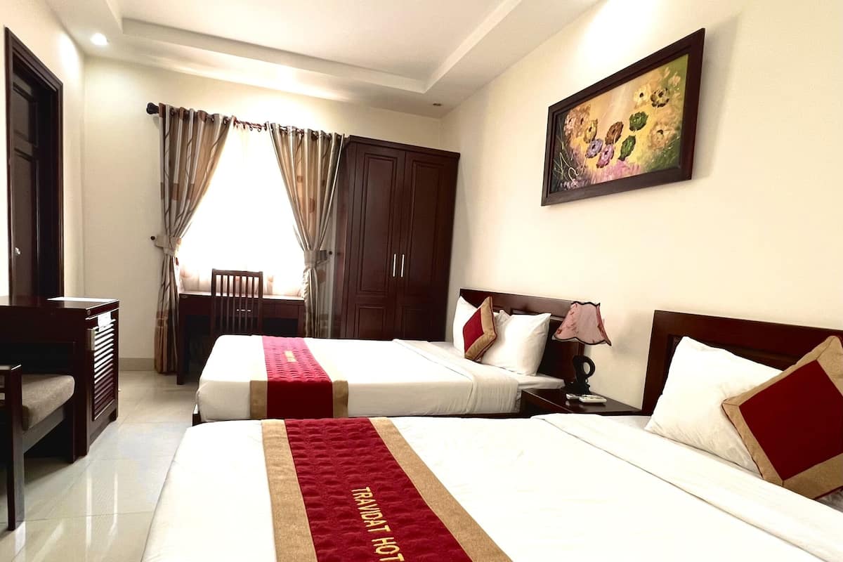 A hotel room with two beds, a desk, a chair, a painting, and a window with curtains.