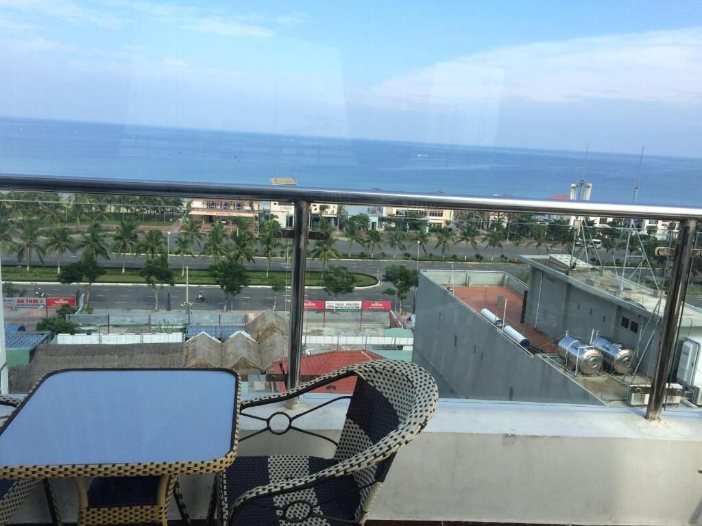 En balkon med et bord og stole, der udover et kystområde med bygninger og palmer.