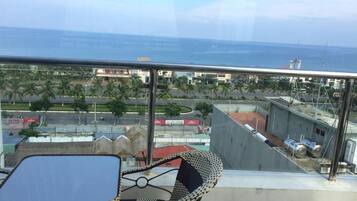 En balkon med et bord og stole, der udover et kystområde med bygninger og palmer.
