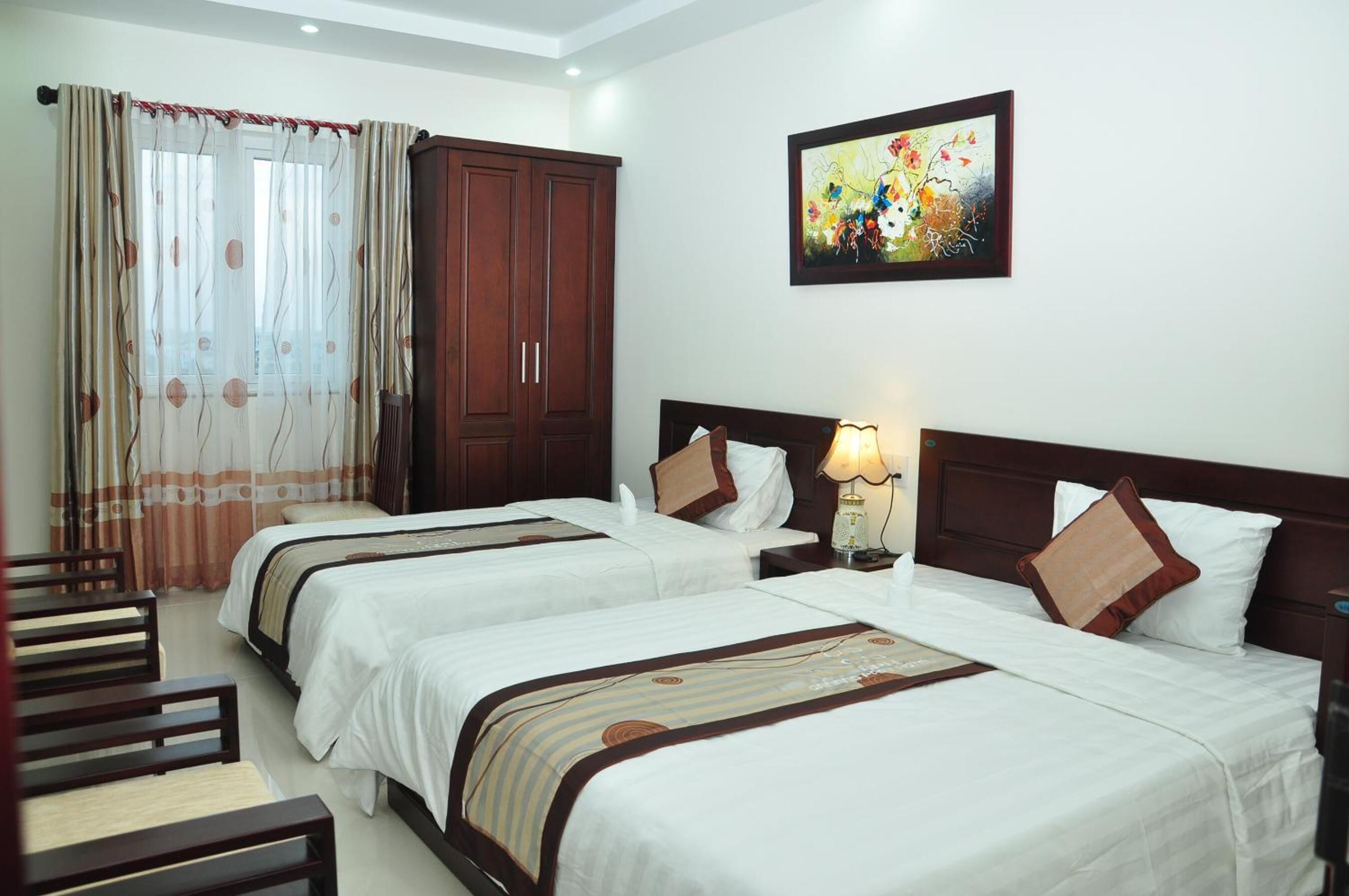A hotel room with two beds, a wardrobe, a painting on the wall, and a window with curtains.