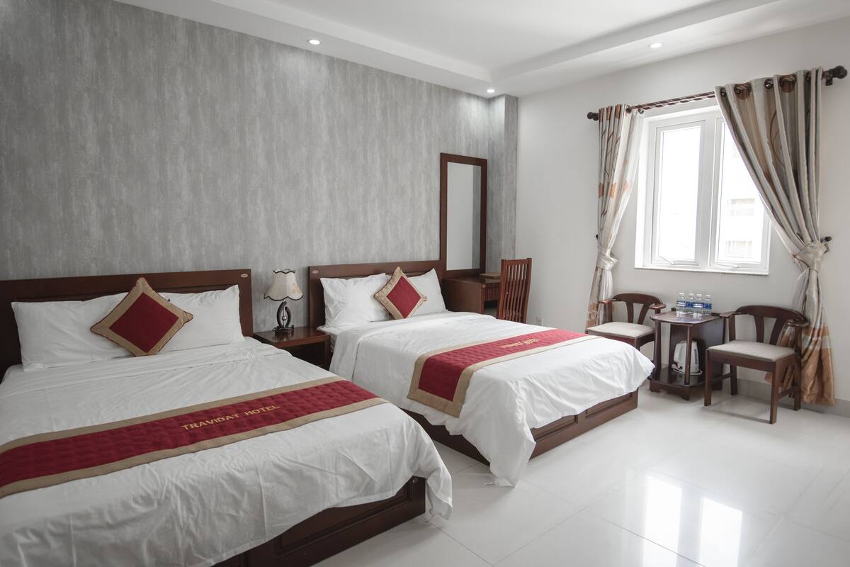 A hotel room with two beds, a small table with chairs, and a window with curtains.