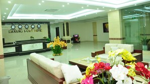 A hotel reception area with a reception desk, seating area, and a clock displaying time in multiple cities. - Dattravi Hostel (Da Nang)