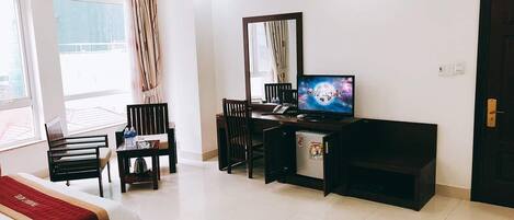 A hotel room with a bed, a desk with a computer, a TV, and a small refrigerator.