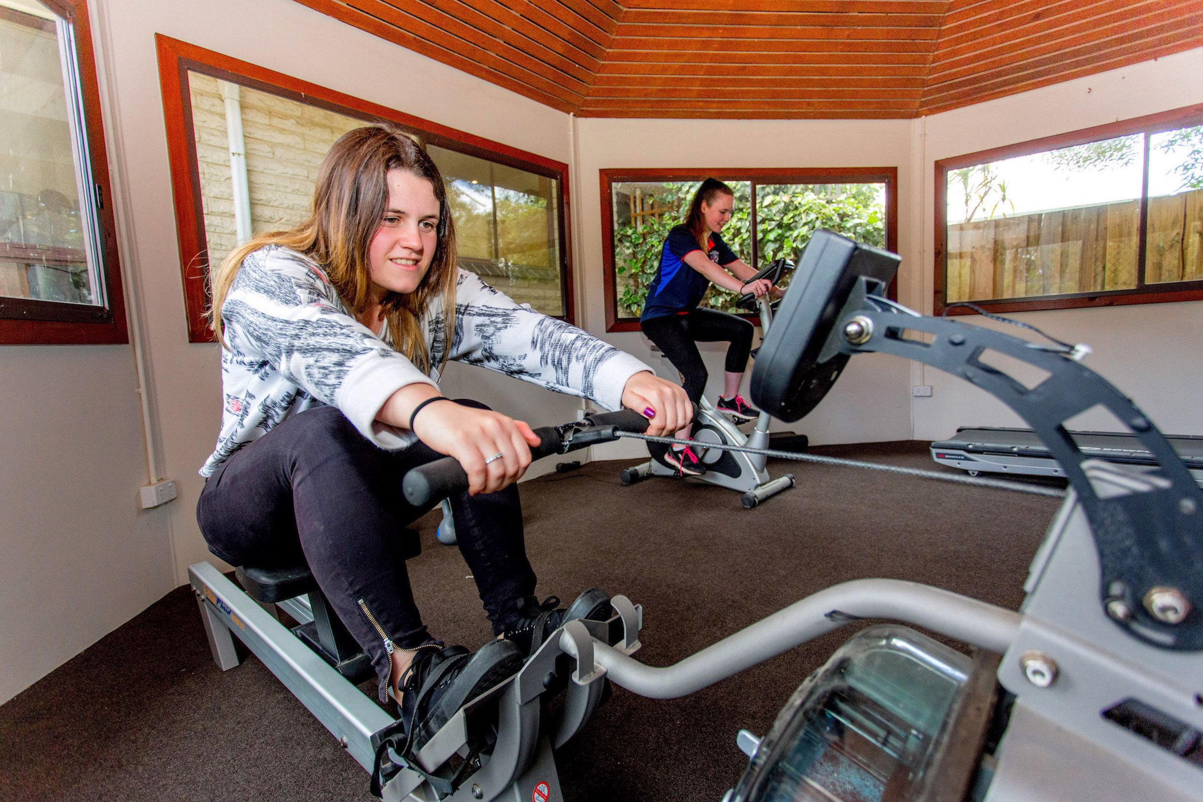 A room with two stationary bikes, large windows, and a wooden ceiling.