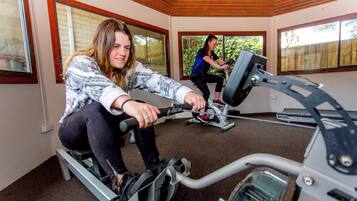 A room with two stationary bikes, large windows, and a wooden ceiling.