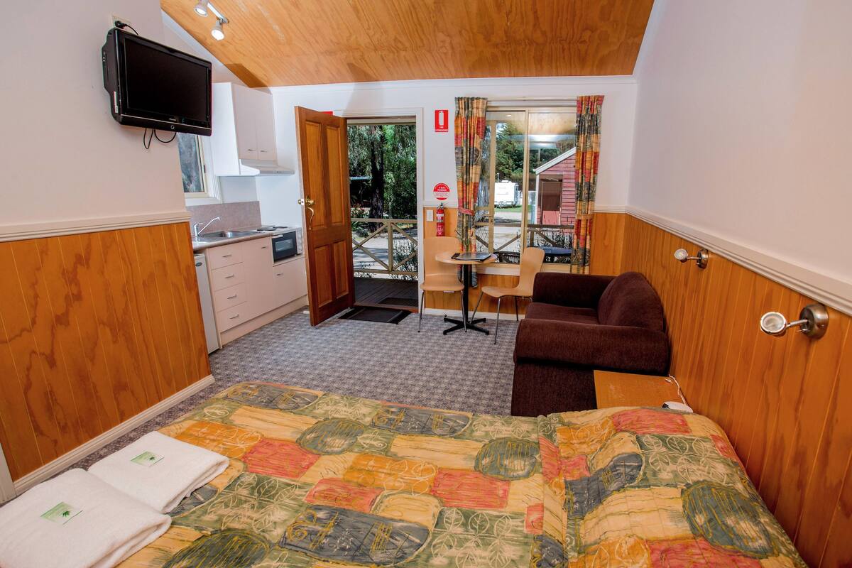 Ein Hotelzimmer mit Bett, Schreibtisch, Sofa, Fernseher und Blick ins Freie.