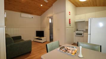 A cozy living room with a sofa, a small TV, and a dining table with magazines and a vase.