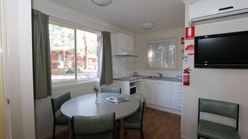 A compact kitchen with white cabinets, a microwave, and a built-in oven. There is a dining area with a round table and four chairs. A flat-screen TV is mounted on the wall.