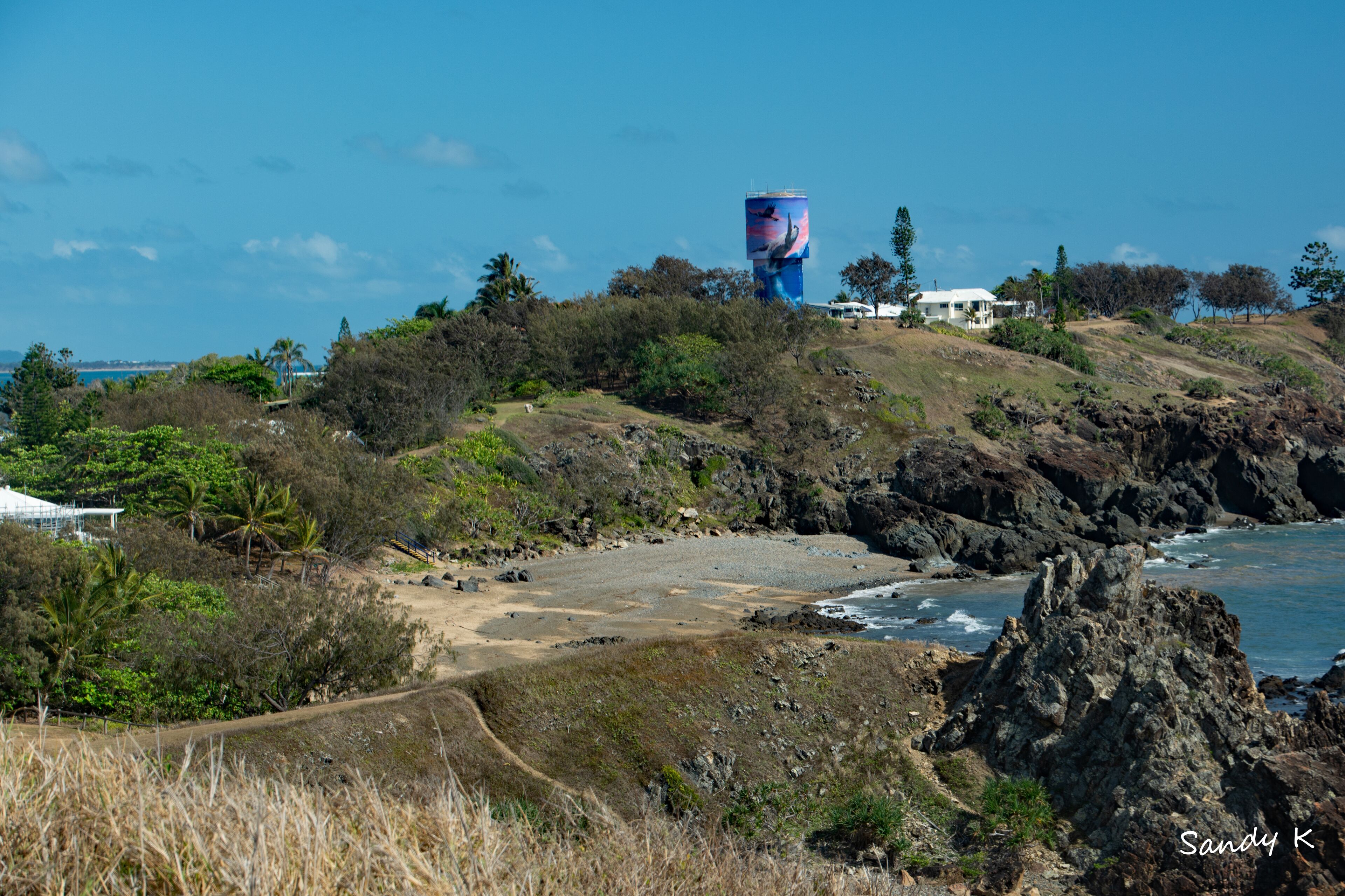 A coastal landscape with a large water tower, rocky terrain, and sparse vegetation.