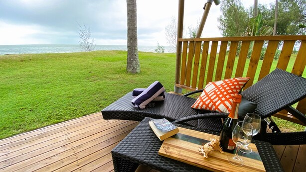 Una terraza de madera con una silla de descanso y una mesa, un libro y una botella de vino.