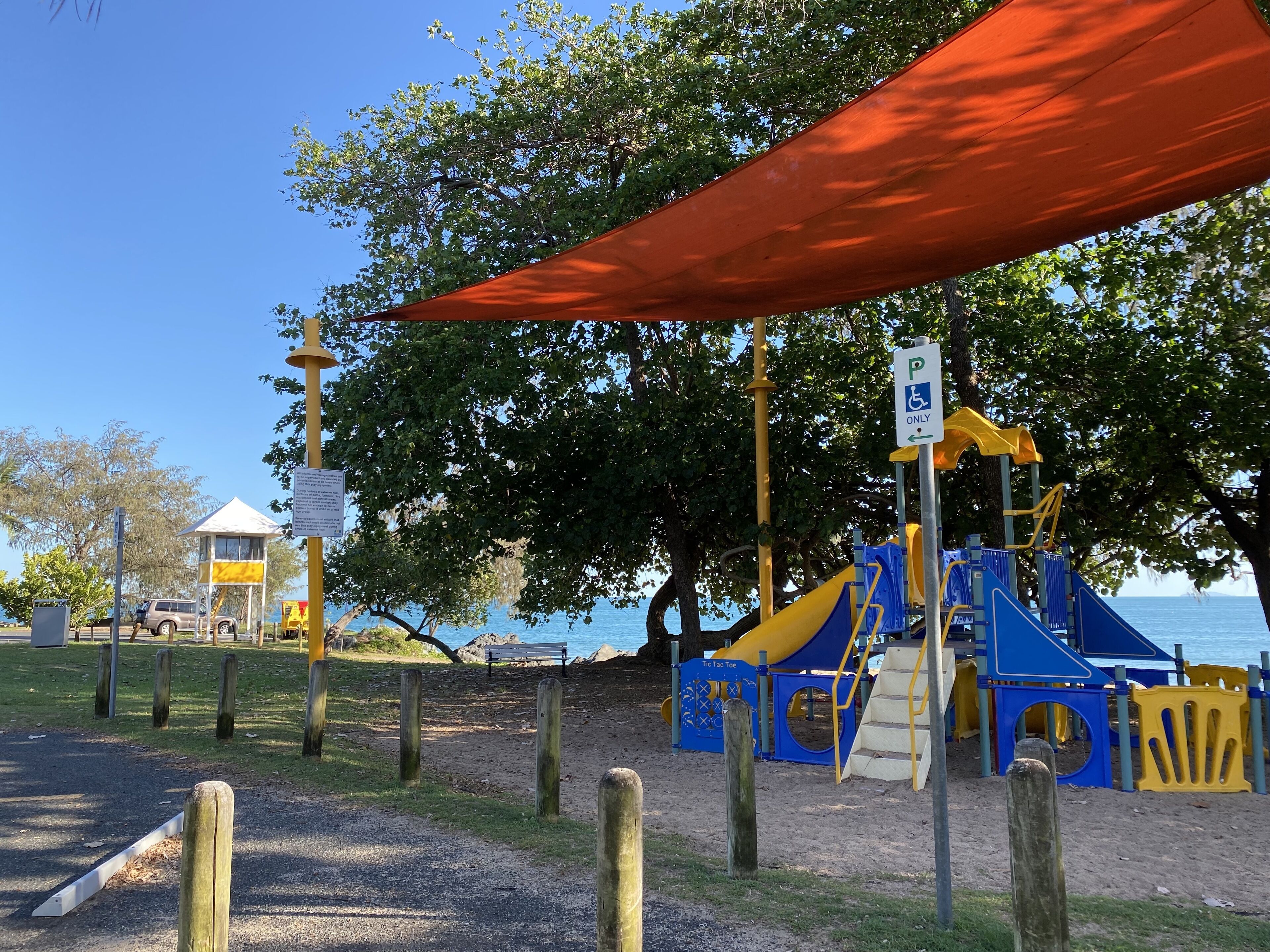 Un espace de jeux avec un toboggan et des structures d’escalade, un espace de repos couvert et une vue sur la mer.