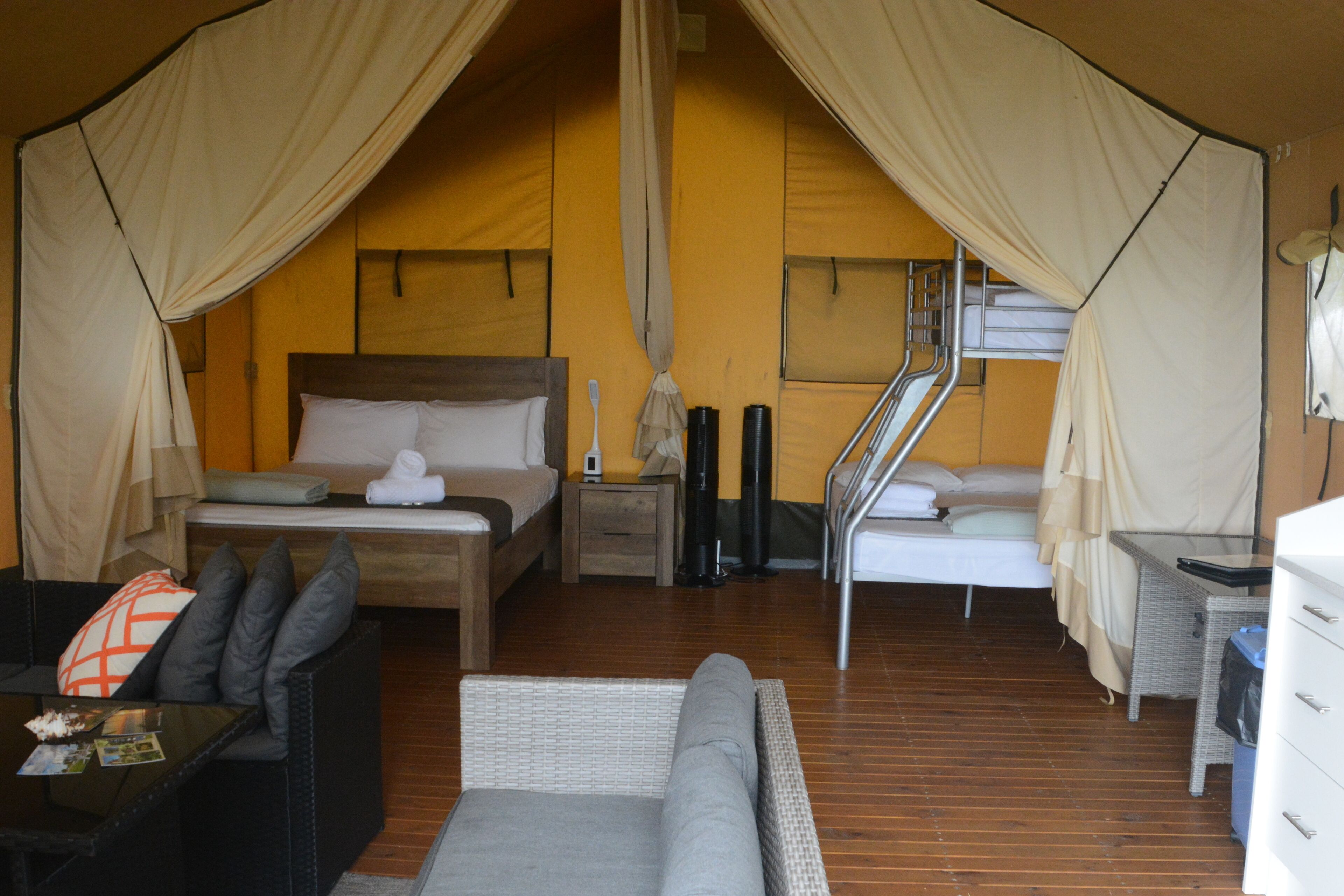 A tented accommodation with a bed, a sofa, a small table, and a chair.