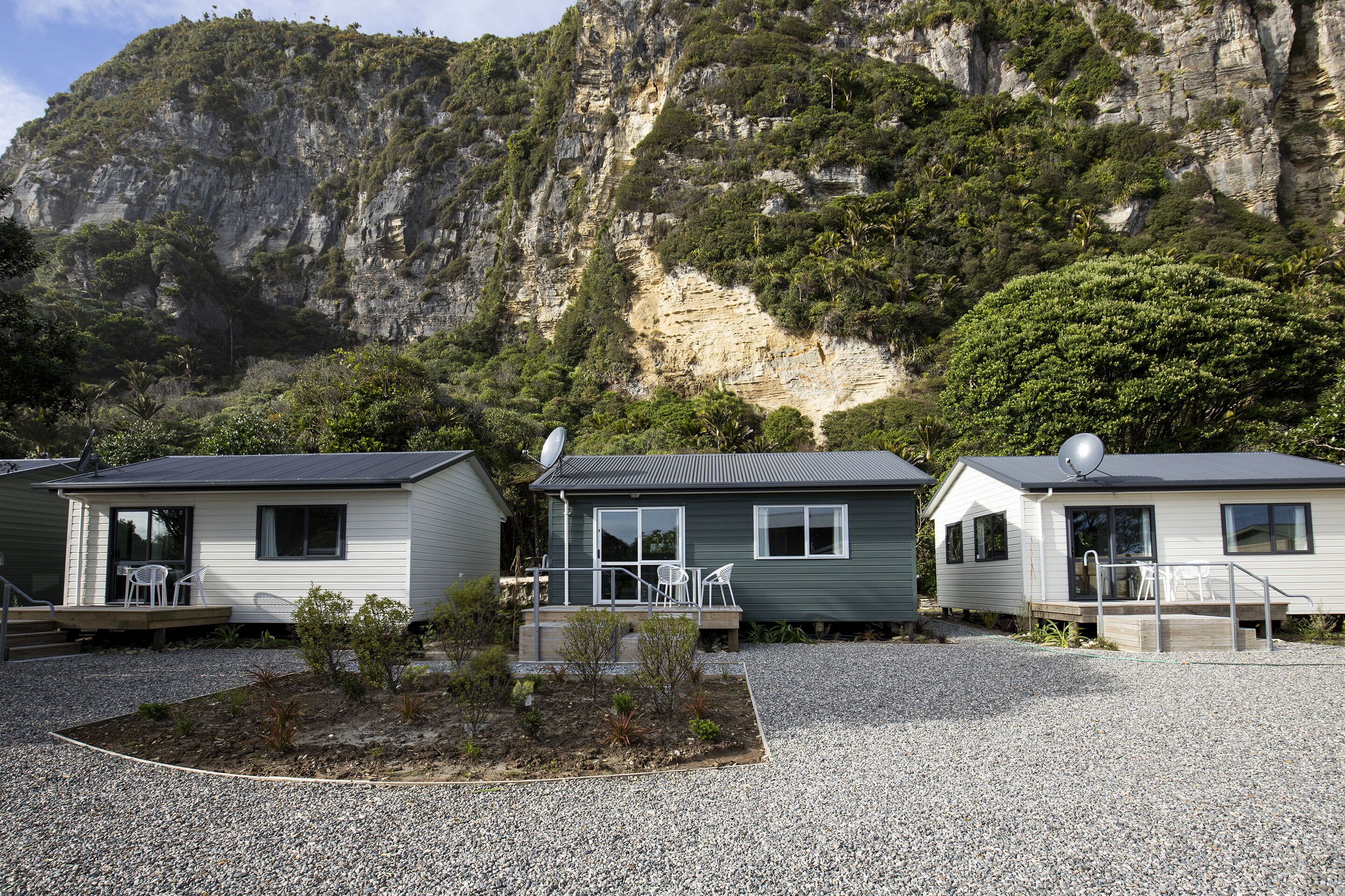 Three cabins with gravel driveways, each with a patio and a satellite dish.