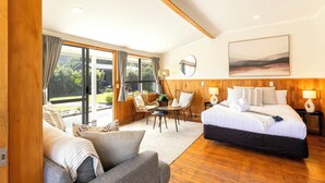 A spacious bedroom with a large bed, a sofa, a dining table, and a view of the outdoors through large windows. - Punakaiki Beachfront Motels (Punakaiki)