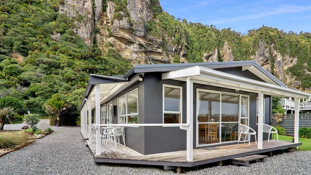 A modern house with large windows, a wooden deck, and a view of a rocky mountain. - Punakaiki Beachfront Motels (Punakaiki)