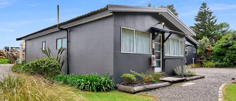 A modern two-story house with a grey exterior, a front porch, and a gravel driveway.